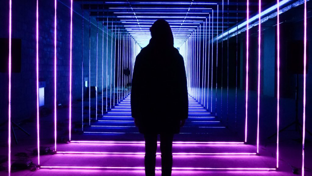 Image of a shadowy figure standing in a neon-lit hallway.