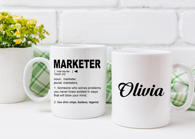2 coffee mugs - 1 says marketer with the dictionary definition underneath. the other says Olivia. great gifts for marketers and copywriters