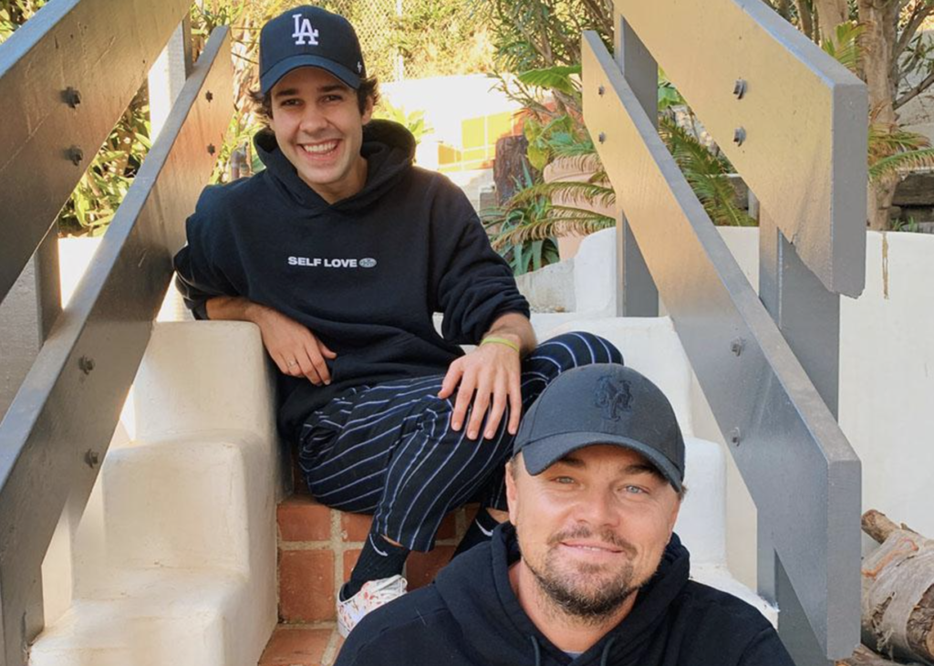 Mega influencer David Dobrik and celebrity actor Leonardo DiCaprio smiling and sitting on stairs
