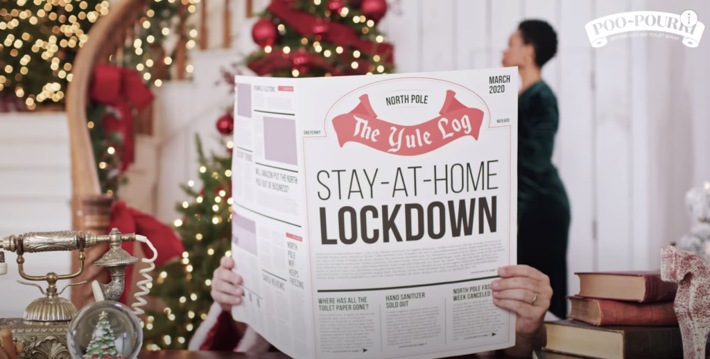 Santa reading a newspaper named The Yule Log with headline Stay-at-Home Lockdown and a black woman as Mrs. Claus in the background decorating a Christmas tree from the Pou-Pourri holiday marketing campaign