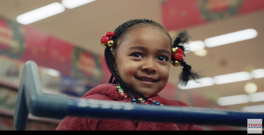 A young black girl smiling mischievously in a shopping cart at UK grocery store Tesco